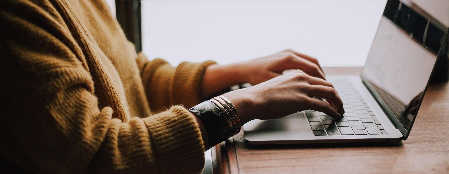 woman types on her laptop near large window